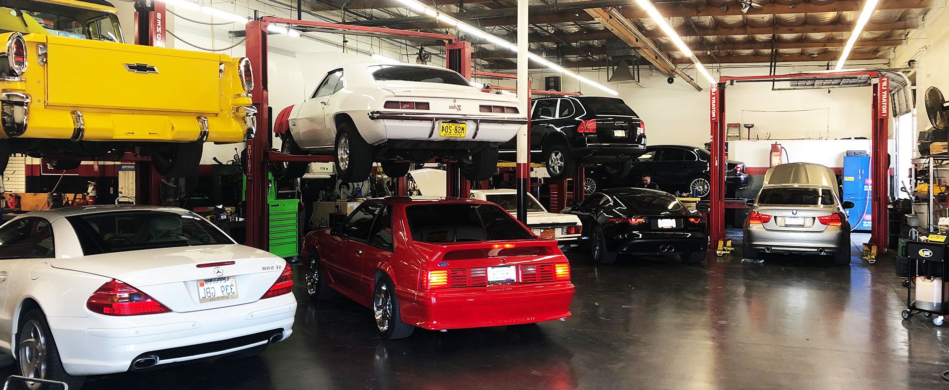 Airpark Auto Clinic performance shop in Scottsdale featuring classic and modern vehicles on lifts, showcasing custom performance upgrades, engine work, and high-end automotive service in a professional garage environment