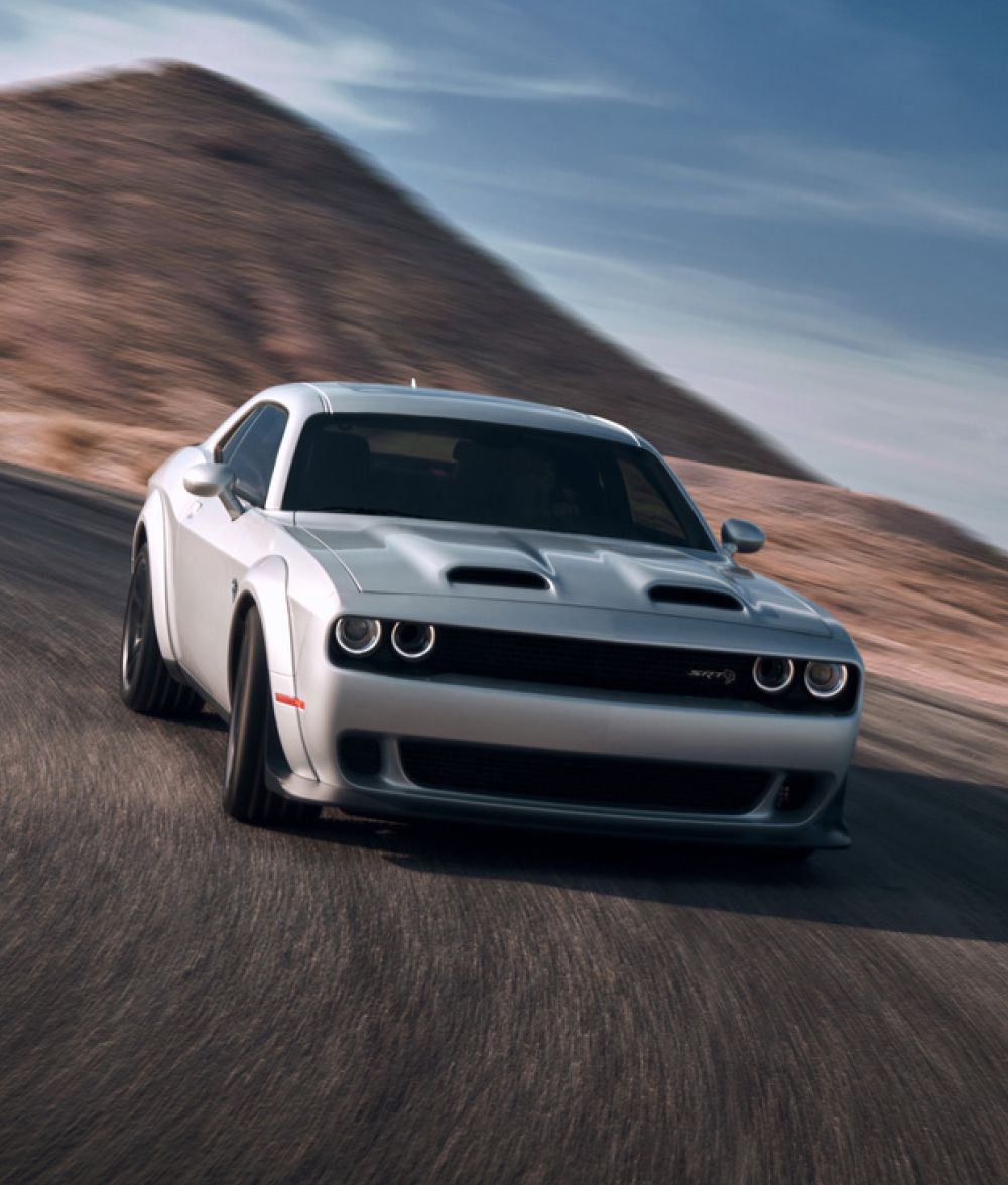 A silver Dodge Challenger drives down a curvy desert road