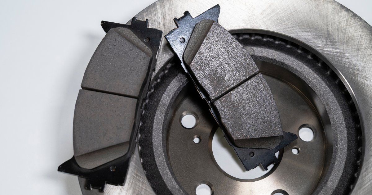 A worn brake pad and a brand-new brake pad are both sitting on top of a new clean metal brake rotor.