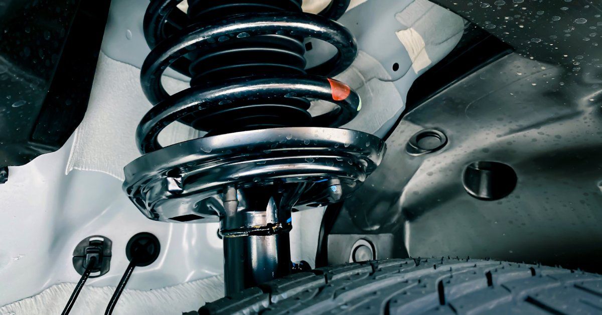 The silver spring coil of a vehicle’s suspension system. Below the spring is a tire that looks clean and undamaged.