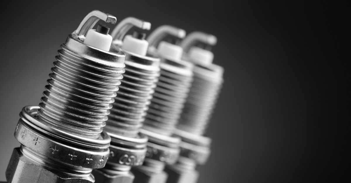 Four small, clean silver spark plugs are upright and next to each other in a straight line against a black backdrop. Four small, clean silver spark plugs are upright and next to each other in a straight line against a black backdrop.
