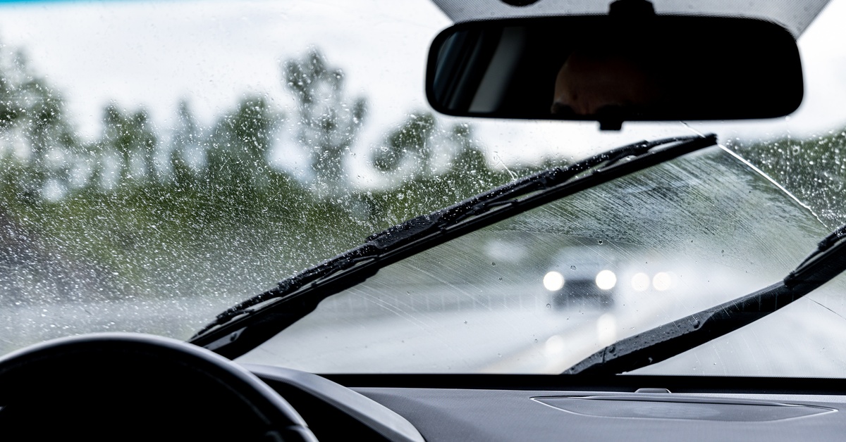 Two wiper blades are moving across the windshield of a car that is covered in rain. Two cars are in the oncoming lane.