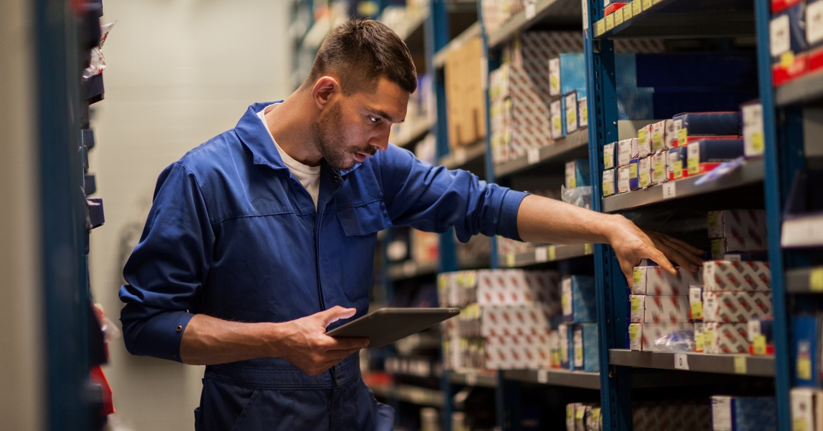 An employee wearing a blue shirt is checking products on the shelf while holding a tablet in their hand.