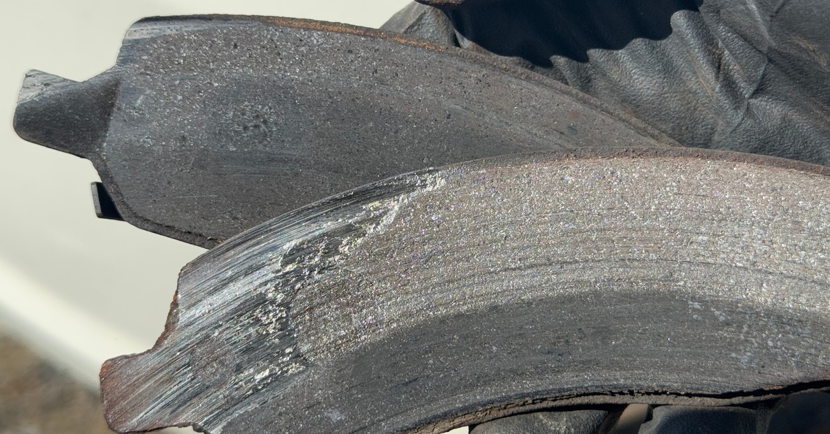 Someone holding slick black gloves is holding two brake pads in their hands. One of the brake pads is severely worn.