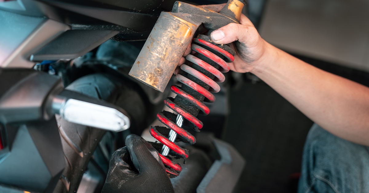 A person is holding a red shock absorber in their hand. One hand has a black glove and the other does not have a glove.
