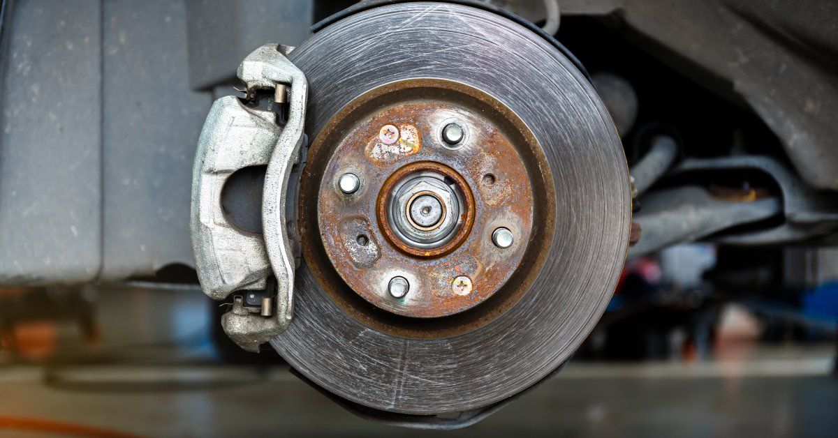 A metal brake rotor on a car that is not attached to a tire. The rotor is heavily scratched on its side.
