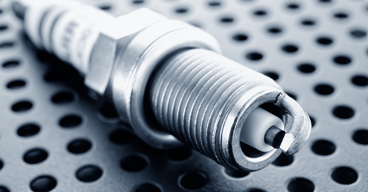 A clean spark plug is lying down on a gray metal surface. The metal surface has small holes evenly spread across it. A clean spark plug is lying down on a gray metal surface. The metal surface has small holes evenly spread across it.