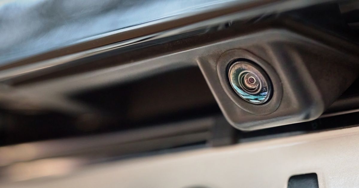 A very small black rearview camera installed at the back of a car. The camera is directly above the license plate.