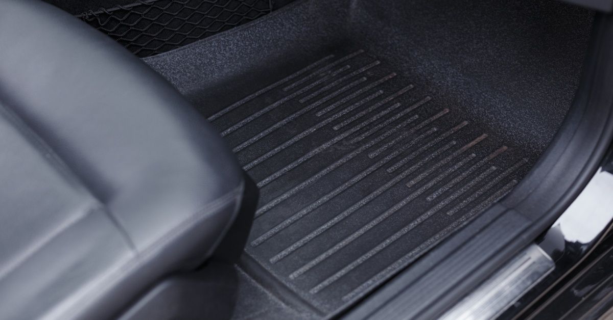A floor mat with raised strips on its surface is installed inside of a car. The floor mat is black and looks clean.