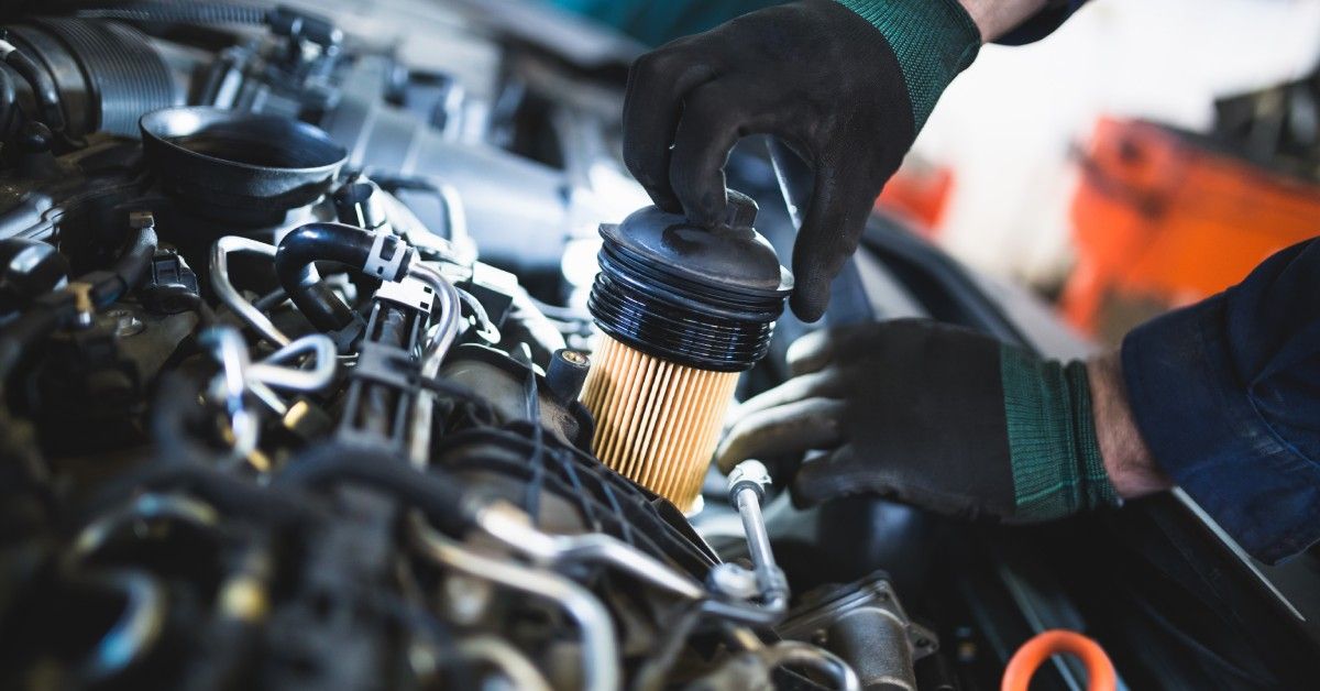 A person wearing gloves is placing a new oil filter inside of a vehicle. The new oil filter is completely clean. A person wearing gloves is placing a new oil filter inside of a vehicle. The new oil filter is completely clean.