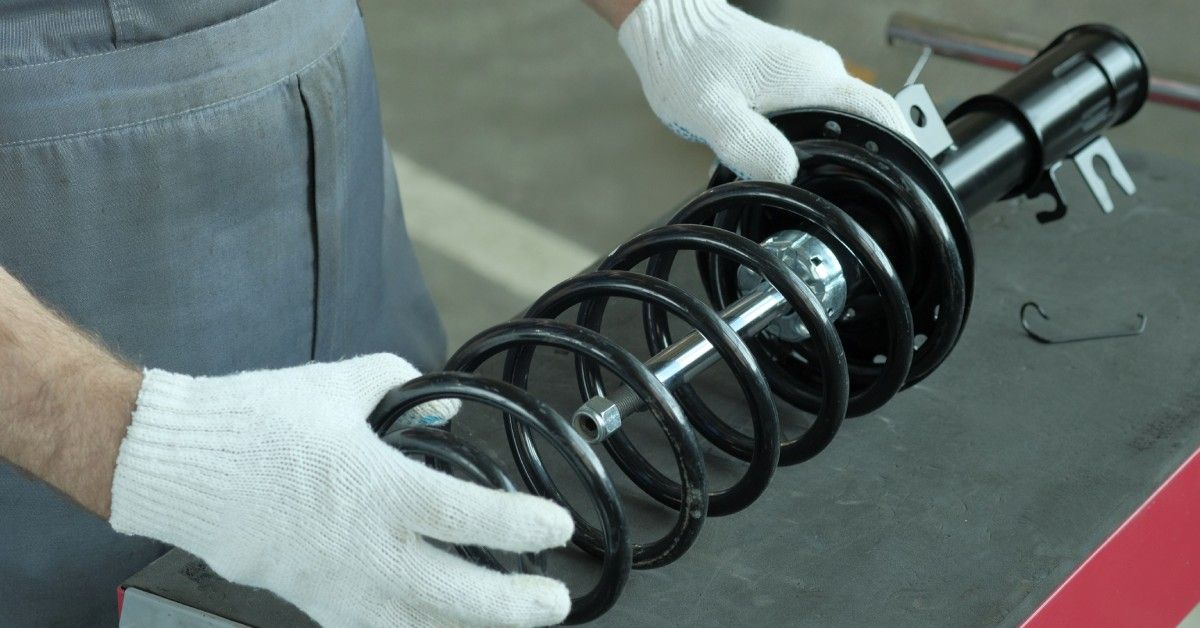 A person wearing white gloves holds a clean coil spring for a car suspension system. The coil is on a small counter. A person wearing white gloves holds a clean coil spring for a car suspension system. The coil is on a small counter.
