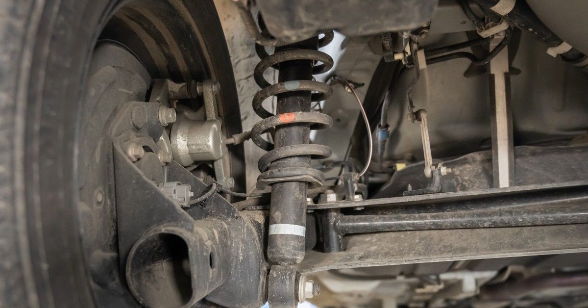 A coil spring and shock absorber attached to a tire on a car. Specks of mud cover the tire and suspension parts. A coil spring and shock absorber attached to a tire on a car. Specks of mud cover the tire and suspension parts.