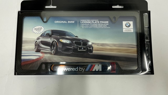 82125A1C497 - Exterior: License Plate Frame, Powered By M for BMW: 230i, 320i, 328d, 330e, 330i, 330i GT xDrive, 340i, 340i GT xDrive, 430i, 430i Gran Coupe, 440i, 530i, 535i GT, 540i, 550i GT xDrive, 640i, 640i Gran Coupe, 640i xDrive Gran Turismo, 650i, 650i Gran Coupe, 740i, 750i, 840i, 840i Gran Coupe, Alpina B6 xDrive Gran Coupe, Alpina B7, M2, M240i, M3, M340i, M4, M440i Gran Coupe, M5, M550i xDrive, M6, M6 Gran Coupe, M760i xDrive, M8, X1, X2, X3, X4, X5, X6, X7, Z4 Image